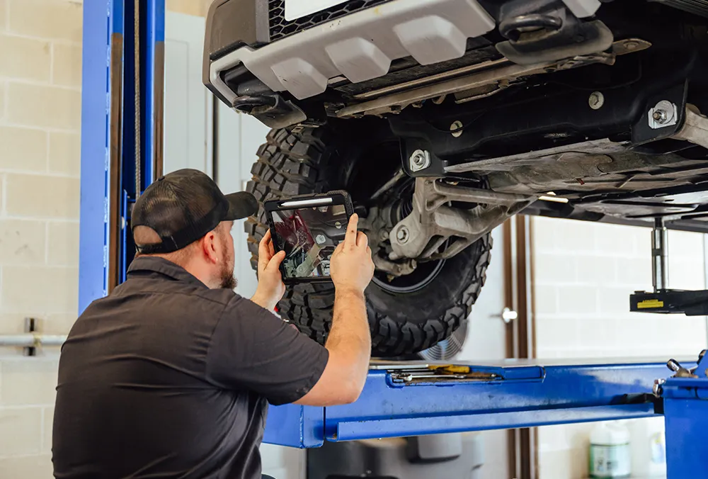 Snider Auto Care technician performing a courtesy check inspection underneath a vehicle